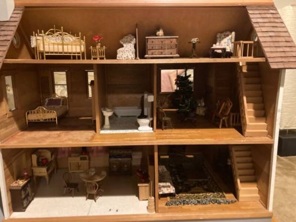 A blue antique dollhouse with brown roof tops white fenced in porch. 7 rooms